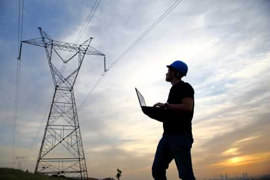 Technician operating laptop beside transmission tower